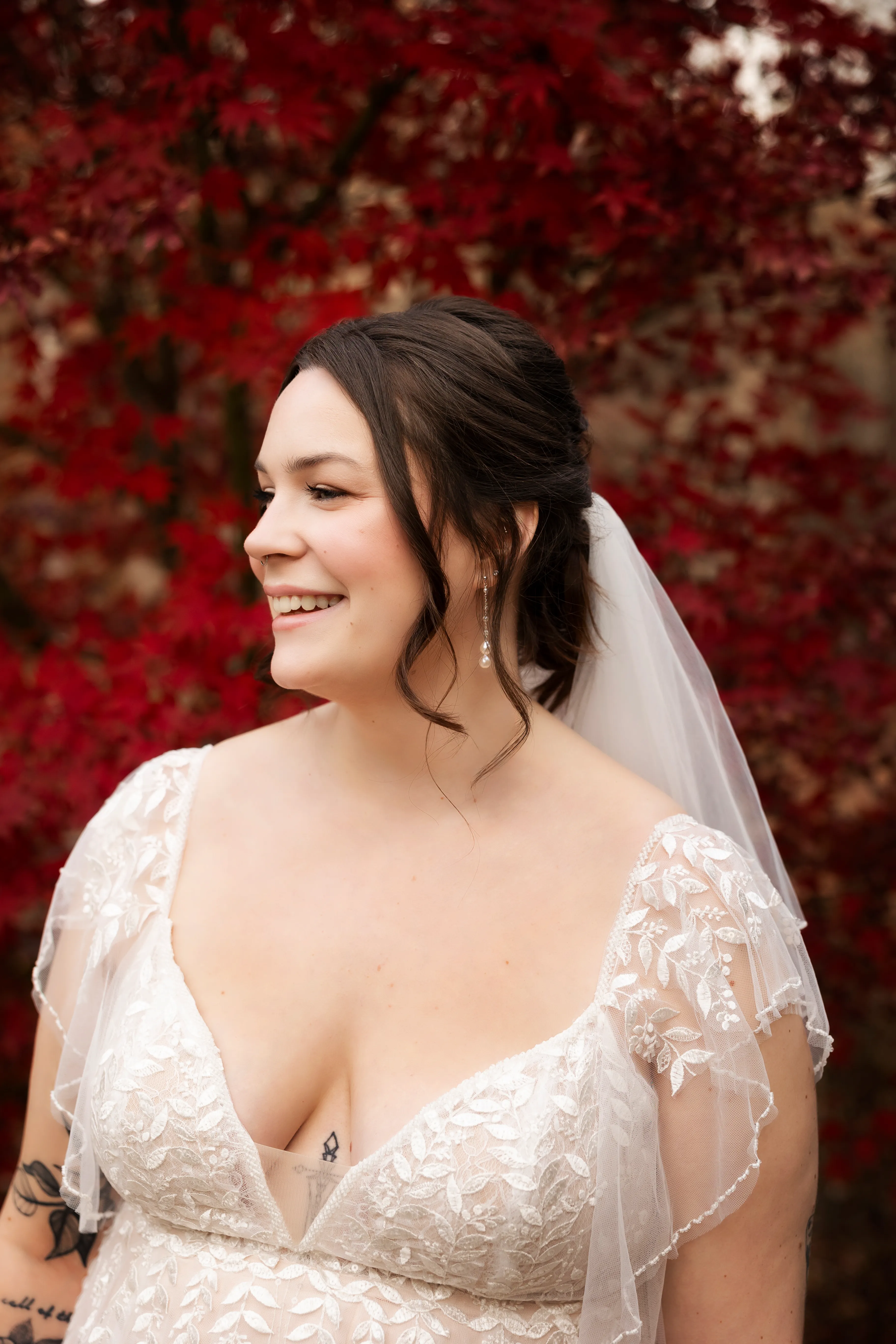 Bride smiling with vibrant red autumn foliage behind her