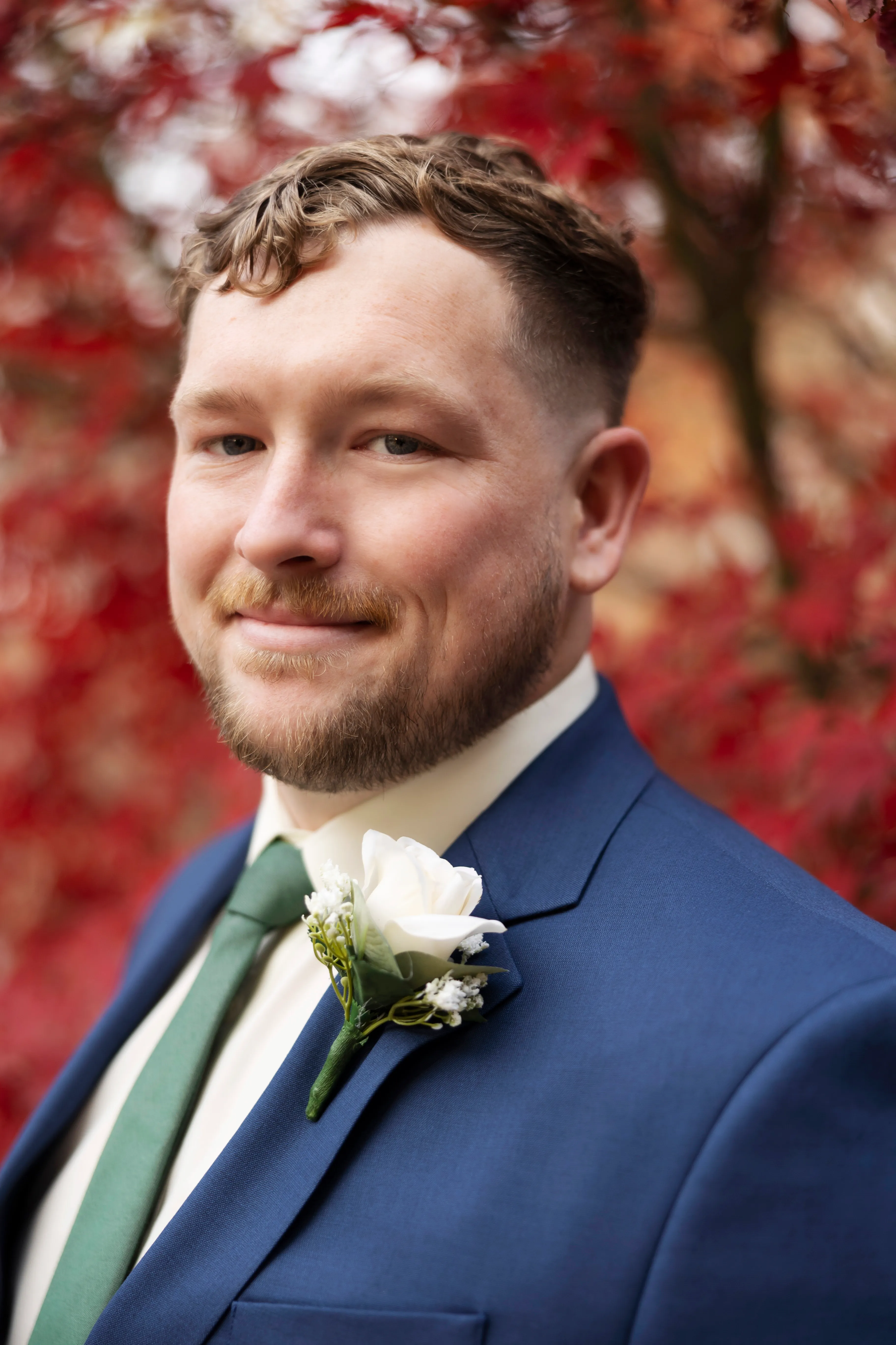 Groom portrait with boutonniere against red autumn foliage