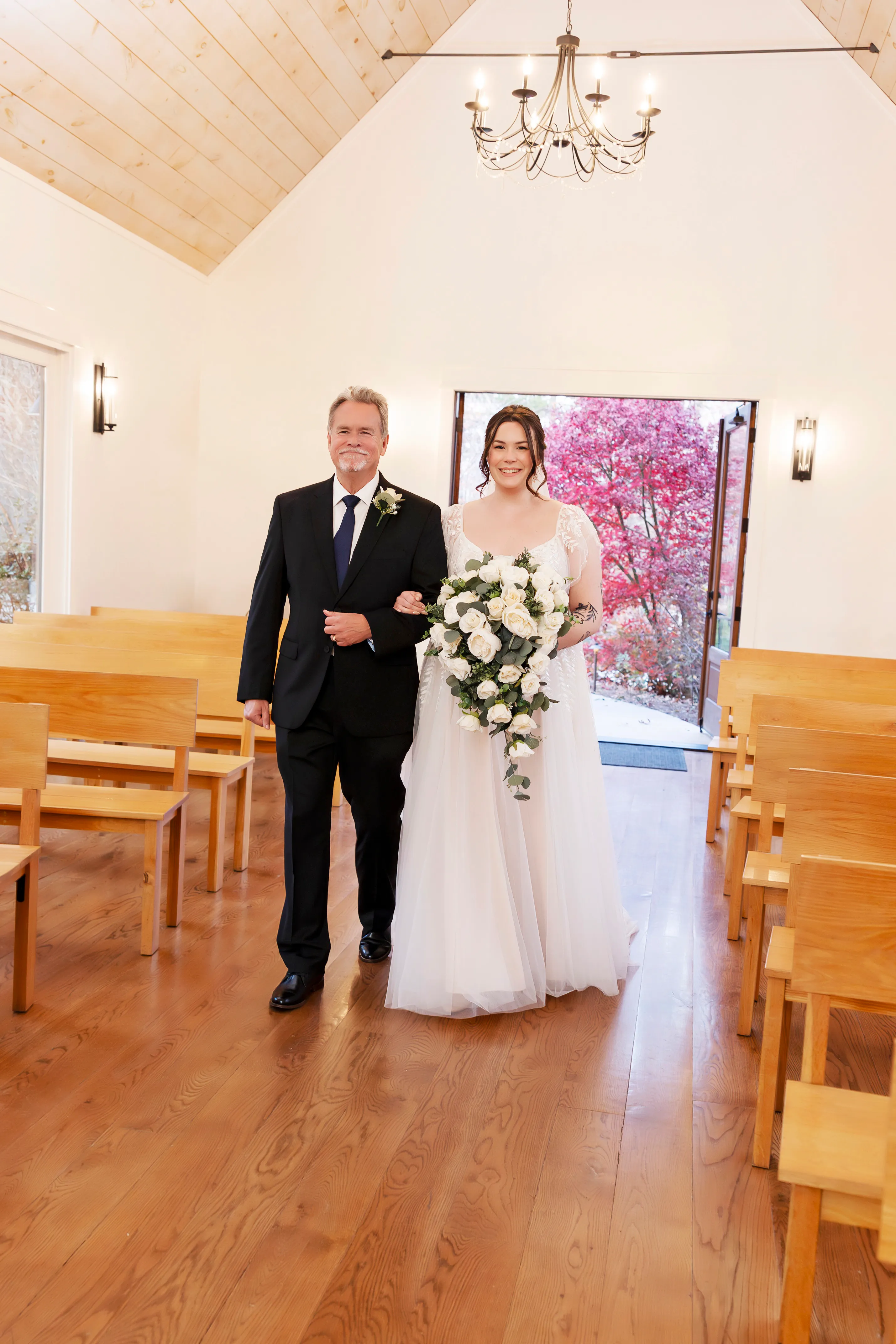 Bride walking down the aisle with her father at Juliette Chapel, holding a white rose bouquet